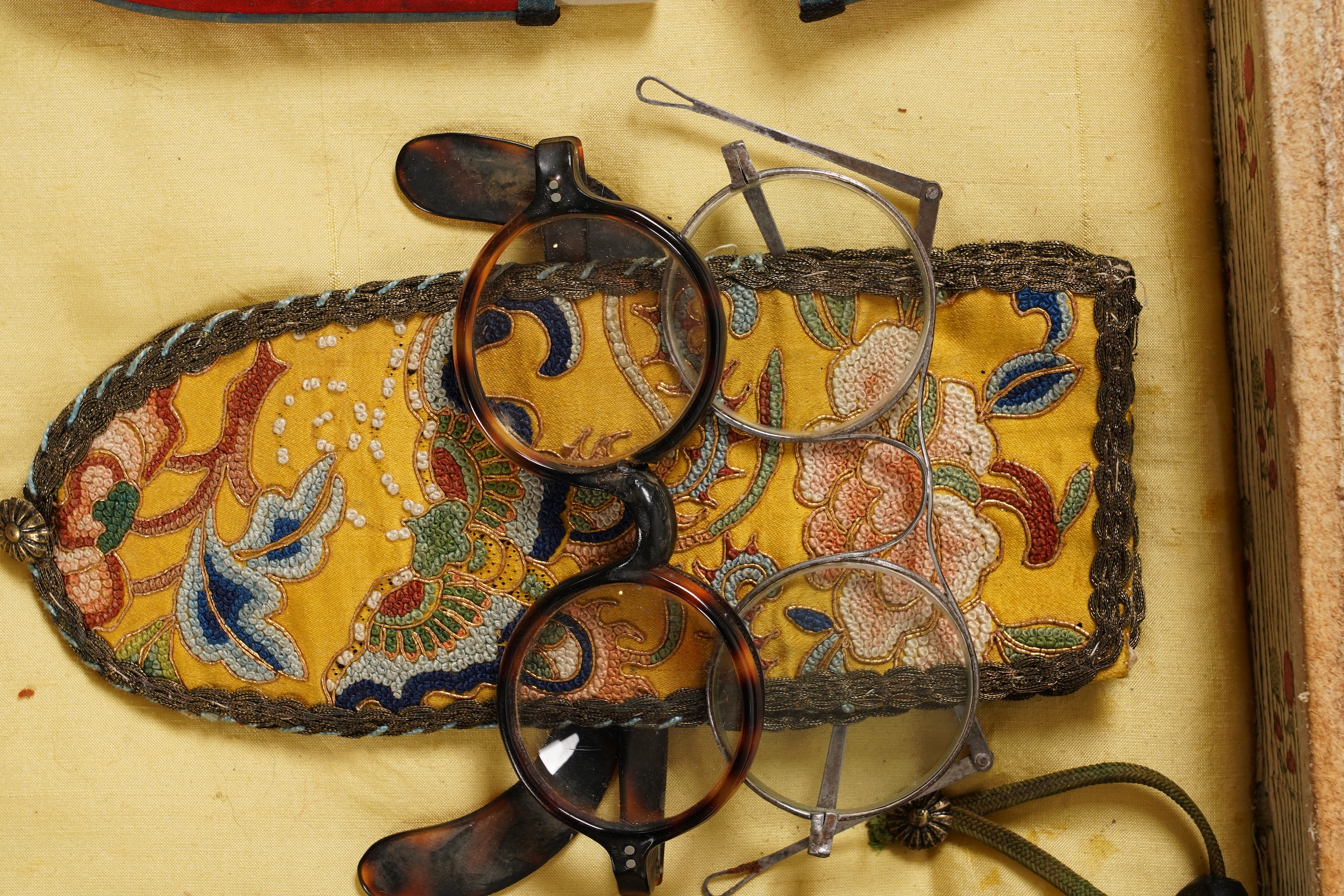 A collection of 19th/20th century Chinese embroidered silk spectacle cases and various spectacles, Box 33cm square